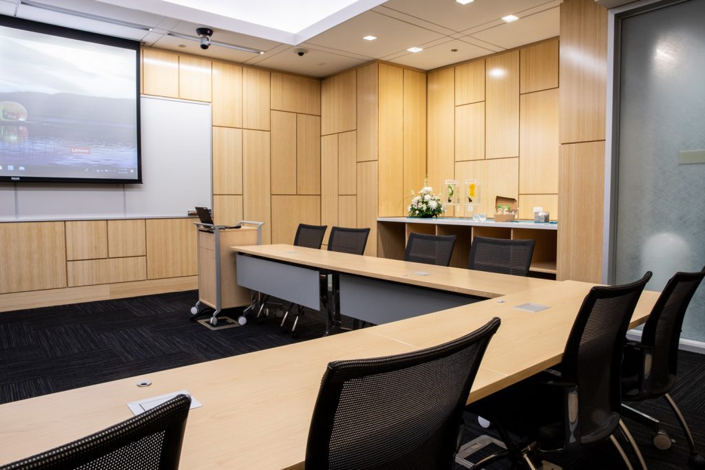 Conference Room 1C at One Rotary Place. Photo of a large conference room with a podium, tables & chairs, a projector, and screen.