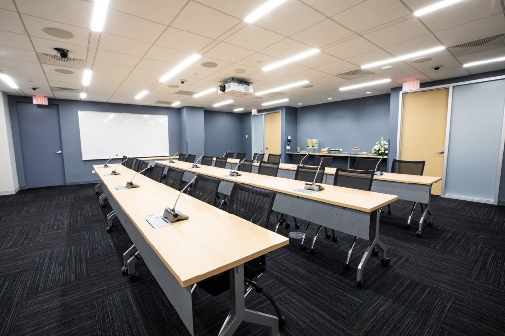 Conference Room 3A at One Rotary Place. Photo of a large conference room with tables & chairs, a projector, and a whiteboard.