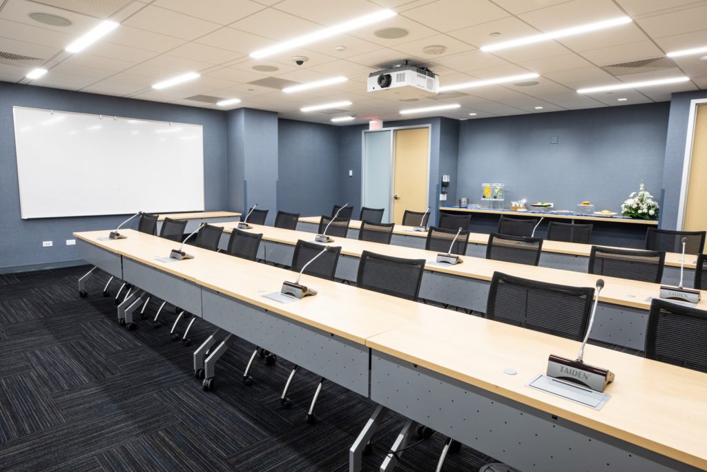 Conference Room 3A at One Rotary Place. Photo of a large conference room with tables & chairs, a projector, catering, and a whiteboard.