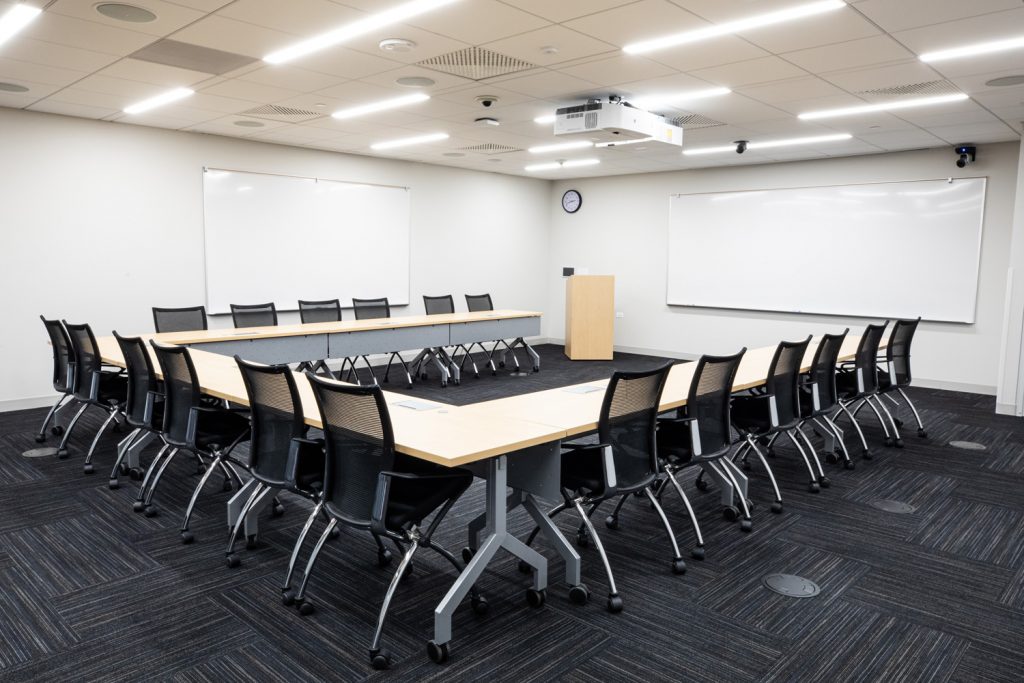 Conference Room 3B at One Rotary Place. Photo of a large conference room with tables & chairs, a podium, projector, and multiple whiteboards.