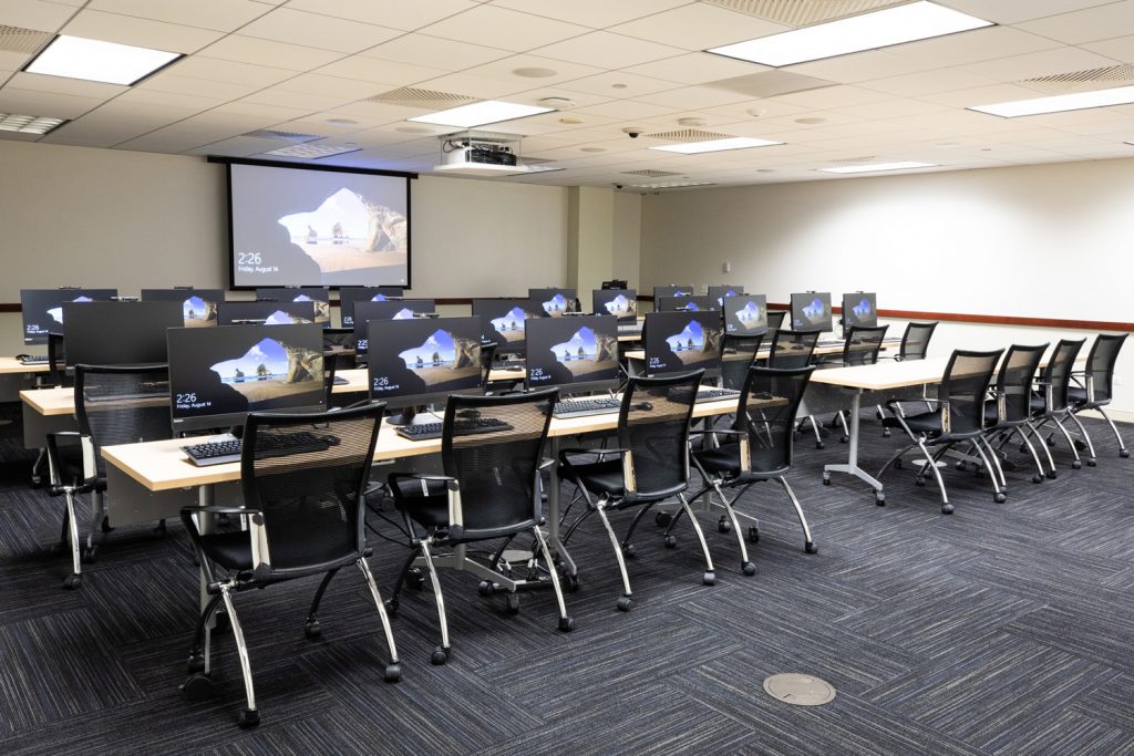 3W Conference Room at One Rotary Place. Photo of a large conference room with tables & chairs, computer stations, a projector, and screen.