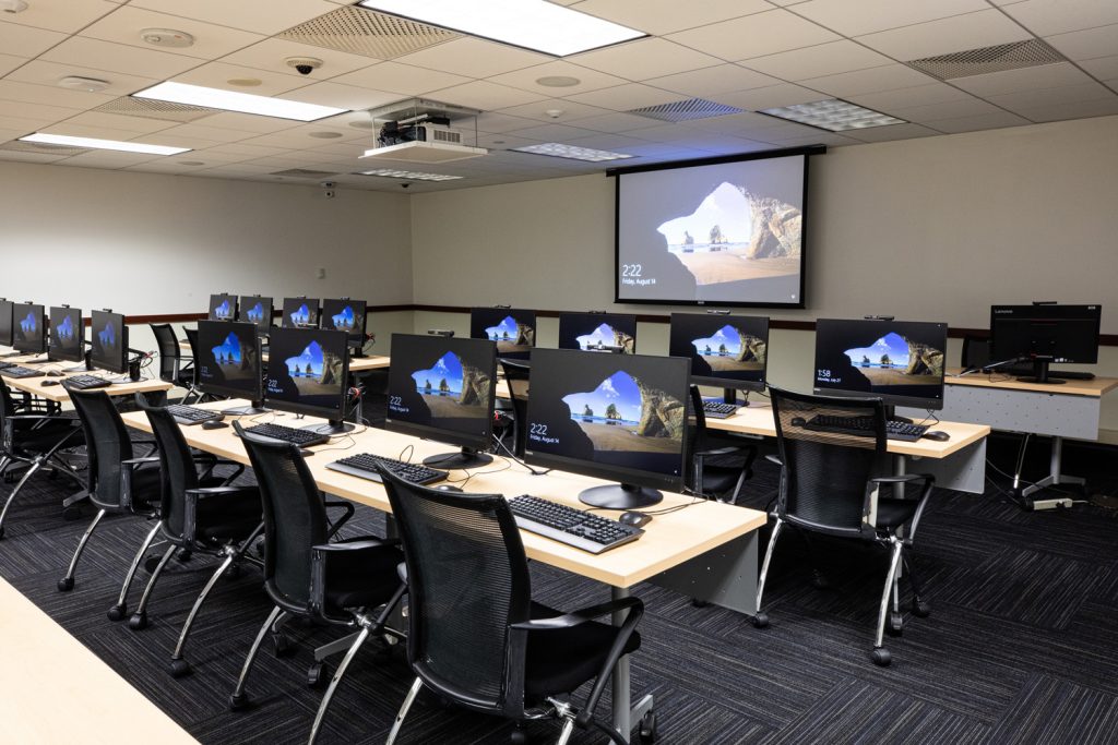 3W Conference Room at One Rotary Place. Photo of a large conference room with tables & chairs, computer stations, a projector, and screen.